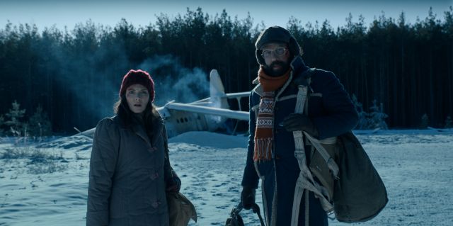 Joyce (Winona Ryder) and Murray (Brett Gelman) look chilly — and worried — in the snow. Perhaps it has something to do with the crashed plane behind them?